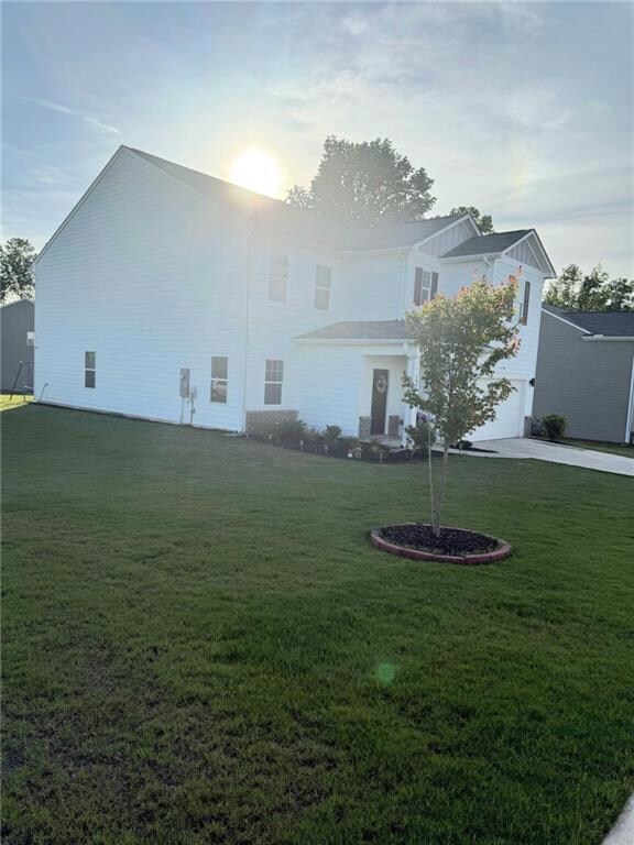 Back of house with board and batten siding, a yard, a garage, and driveway