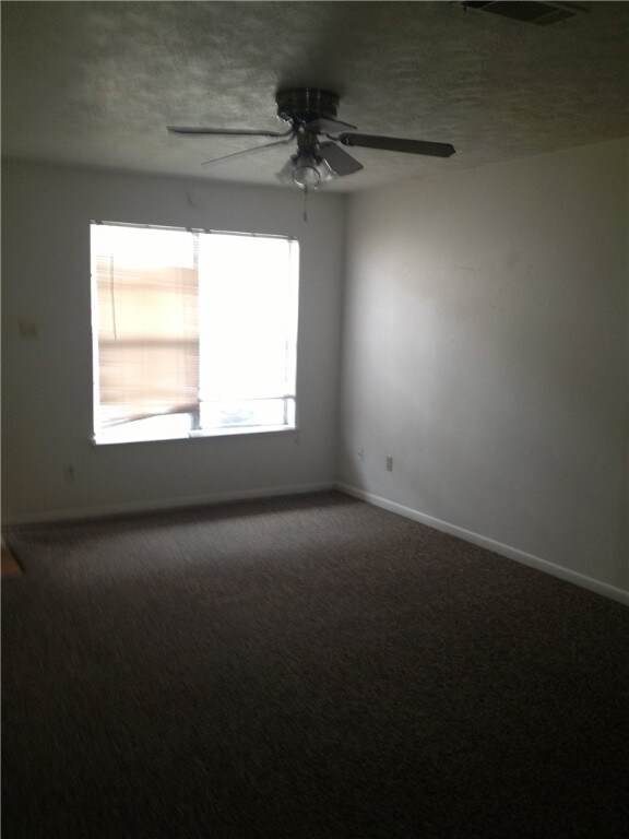 Carpeted spare room featuring a ceiling fan, baseboards, a textured ceiling, and visible vents