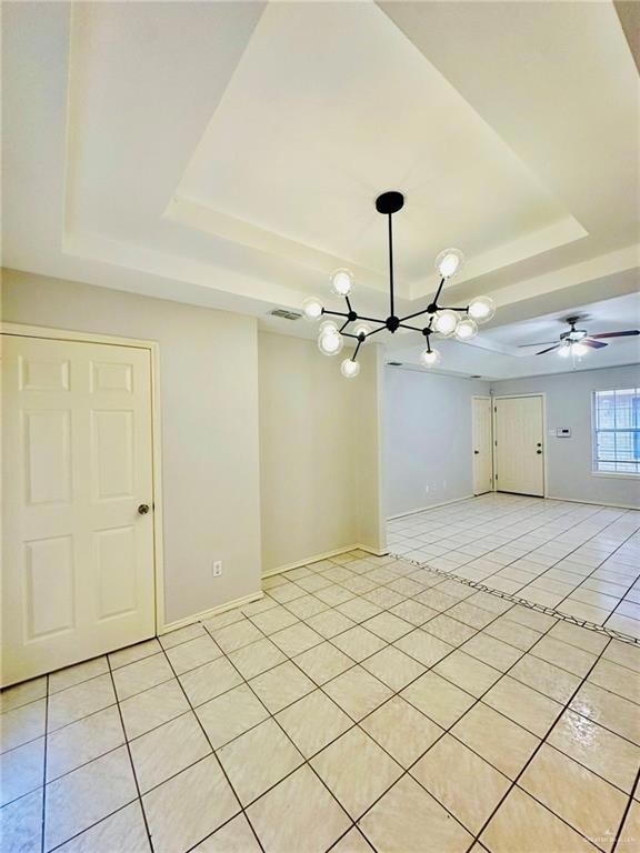 Tiled empty room with ceiling fan with notable chandelier and a raised ceiling