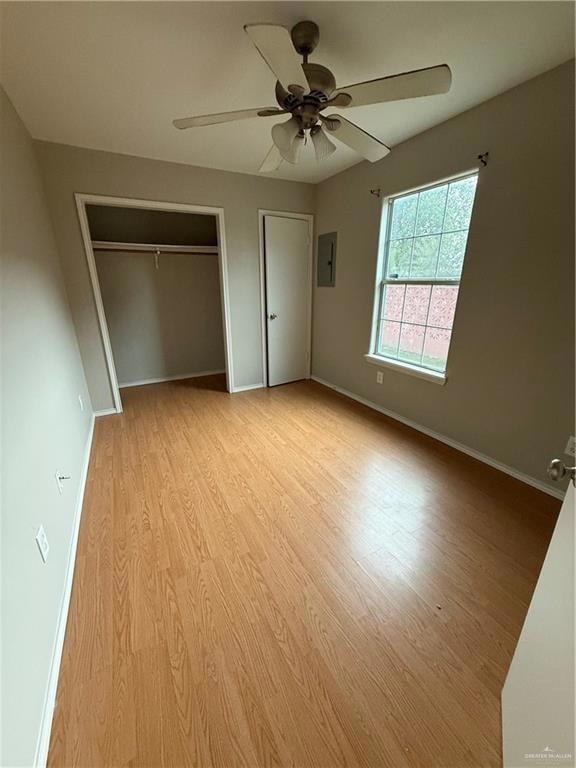 Unfurnished bedroom featuring electric panel, light wood-style floors, baseboards, two closets, and a ceiling fan