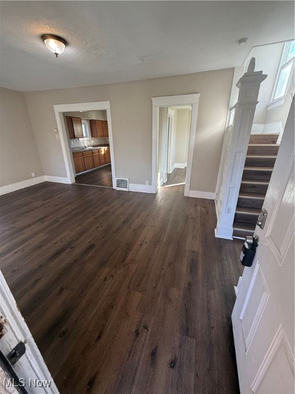 Unfurnished living room featuring dark wood-style floors, stairway, and a textured ceiling