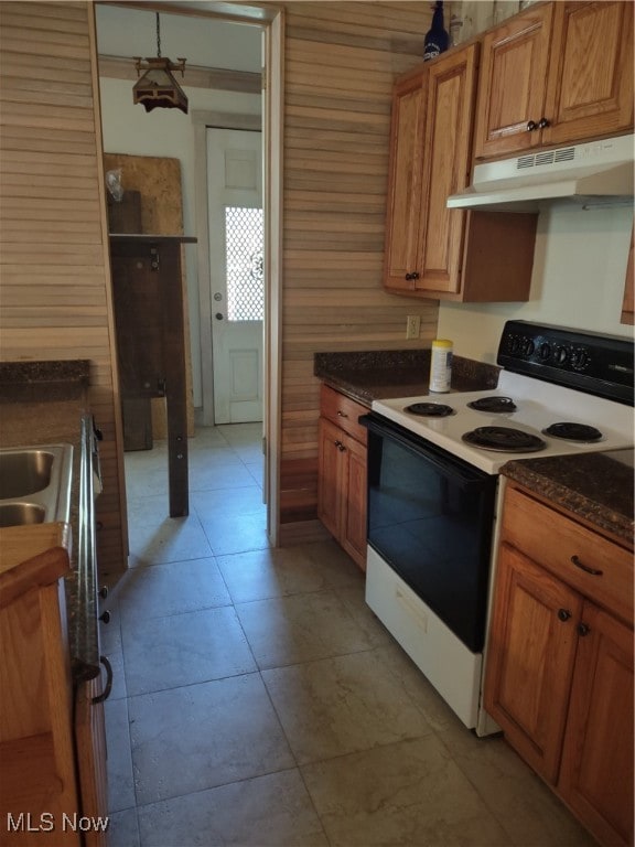 Kitchen featuring stove, brown cabinets, ventilation hood, wood walls, and light tile patterned flooring