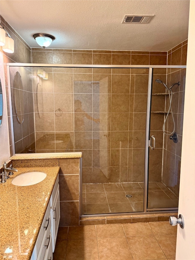 Full bath featuring a textured ceiling, vanity, a stall shower, and tile patterned floors