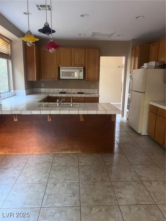 Kitchen with tile counters, pendant lighting, refrigerator, and brown cabinets