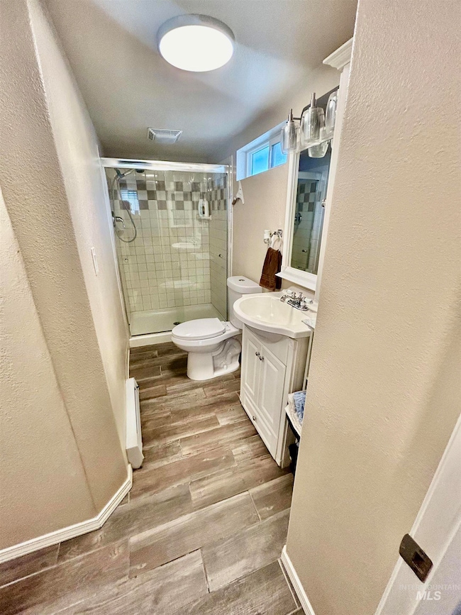 Bathroom featuring vanity, a stall shower, wood finished floors, a textured wall, and a baseboard radiator