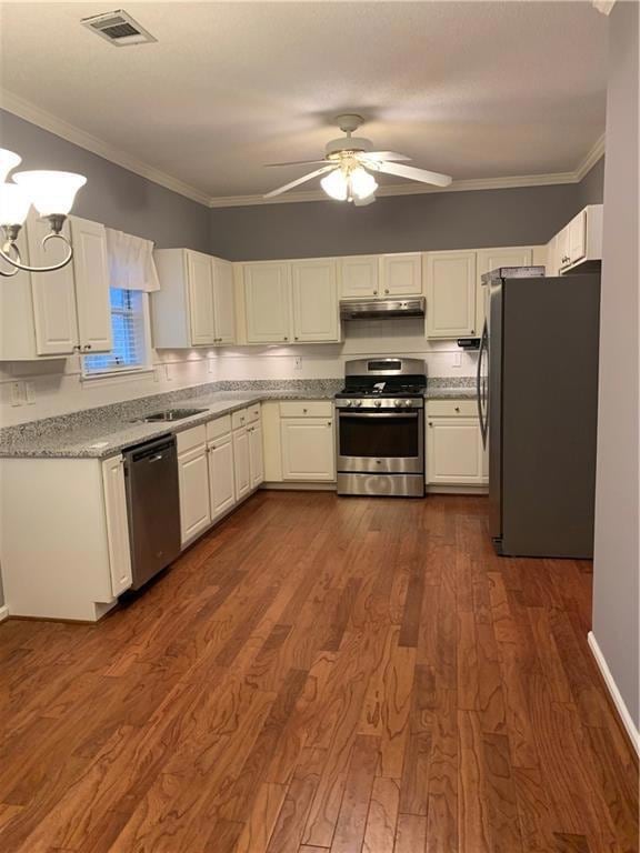 Kitchen featuring appliances with stainless steel finishes, white cabinetry, ornamental molding, a ceiling fan, and dark wood-type flooring