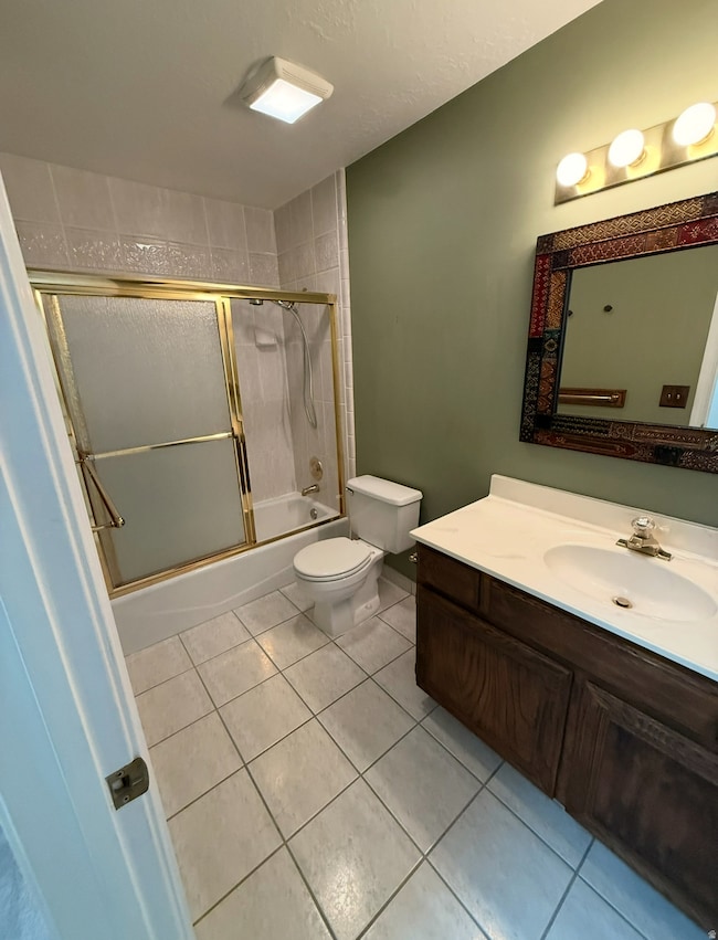 Full bath featuring vanity, light tile patterned floors, shower / bath combination with glass door, and a textured ceiling