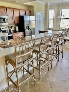 Kitchen featuring crown molding, light stone countertops, a kitchen breakfast bar, brown cabinetry, and appliances with stainless steel finishes