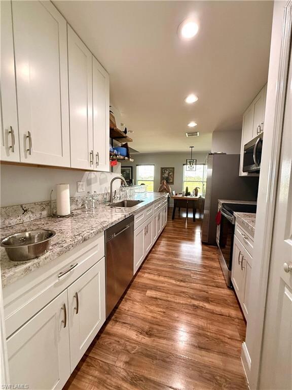Kitchen with white cabinets, appliances with stainless steel finishes, dark wood-style floors, light stone countertops, and recessed lighting