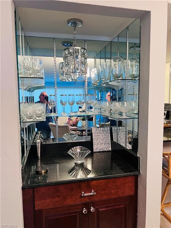 Bar with a textured wall, dark stone counters, dark brown cabinets, and a chandelier