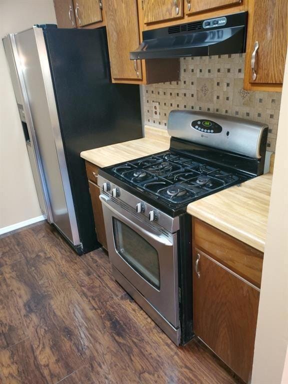 Kitchen featuring stainless steel gas range oven, under cabinet range hood, dark wood-style flooring, light countertops, and tasteful backsplash