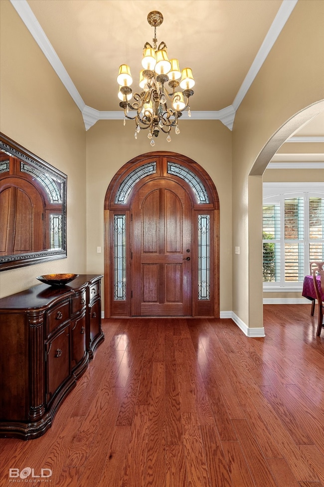 Foyer featuring arched walkways, crown molding, a chandelier, healthy amount of natural light, and wood finished floors