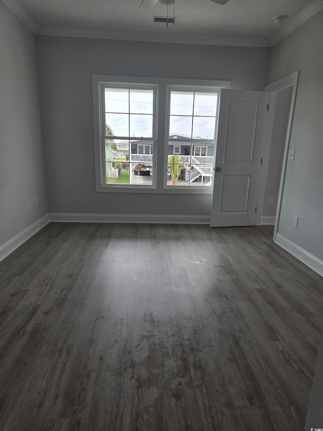 Empty room featuring dark wood-style flooring, visible vents, a wealth of natural light, and ornamental molding