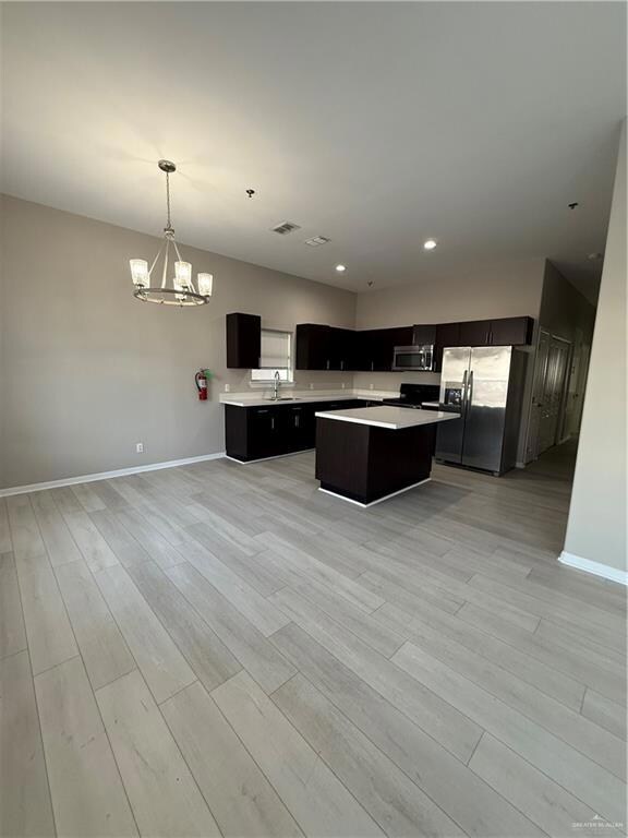 Kitchen featuring refrigerator, light hardwood / wood-style flooring, decorative light fixtures, a kitchen island and a chandelier plus recesed lighting.