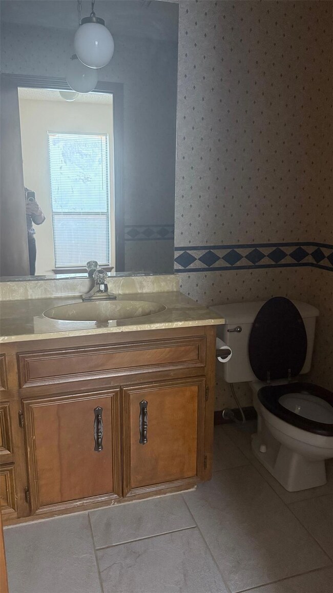 Half bathroom with wallpapered walls, vanity, and light tile patterned flooring