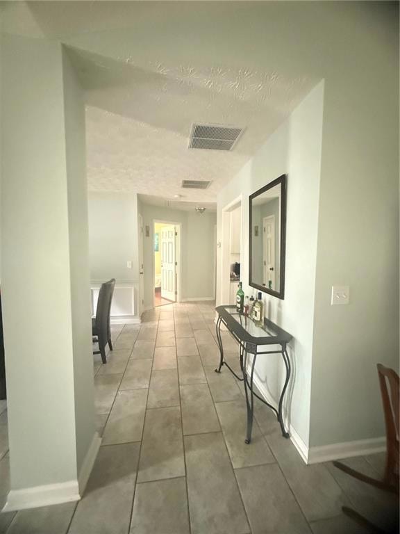Hallway featuring a textured ceiling, tile patterned floors, and baseboards
