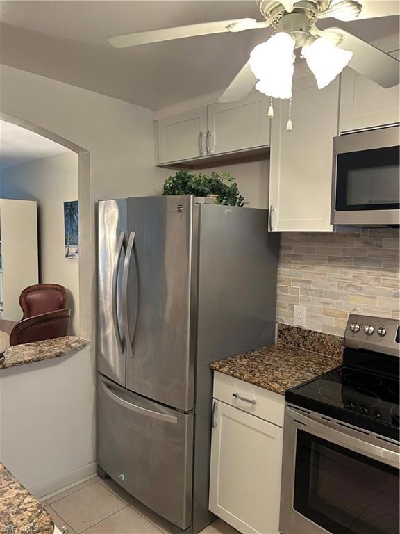 Kitchen featuring range, freestanding refrigerator, a ceiling fan, decorative backsplash, and light tile patterned floors