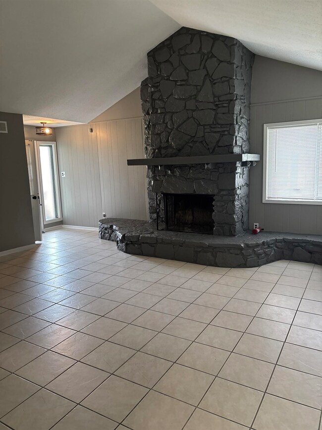 Unfurnished living room featuring lofted ceiling, baseboards, a fireplace, tile patterned floors, and wood walls