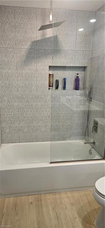 Full bathroom with combined bath / shower with glass door and light wood-style floors