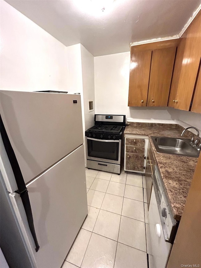 Kitchen featuring freestanding refrigerator, stainless steel range with gas cooktop, brown cabinets, dark countertops, and light tile patterned flooring