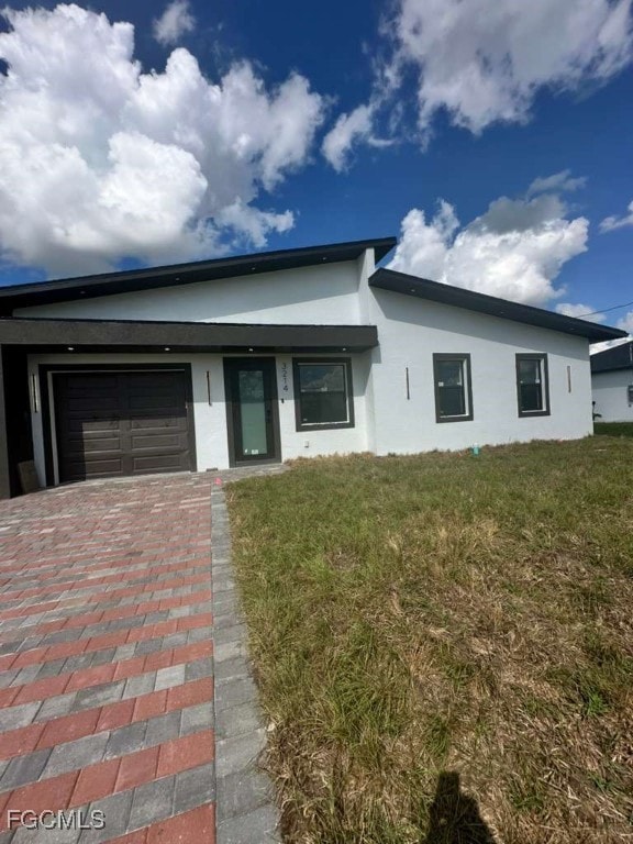 View of front of house featuring a front yard, stucco siding, a garage, and decorative driveway