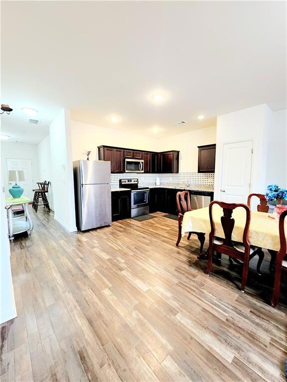 Kitchen featuring stainless steel appliances, tasteful backsplash, light wood-style flooring, dark brown cabinets, and recessed lighting