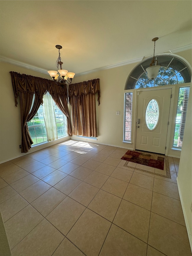 Entryway with light tile patterned floors, crown molding, and a chandelier