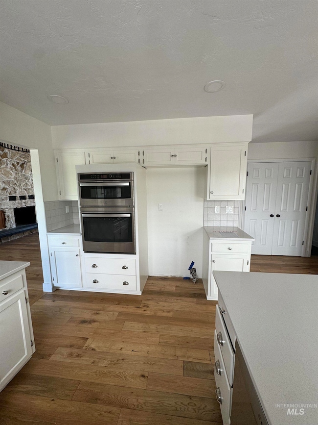 Kitchen featuring double oven, dark wood finished floors, white cabinetry, and backsplash