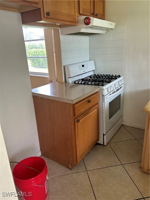 Kitchen with tasteful backsplash, light tile patterned flooring, range hood, and range