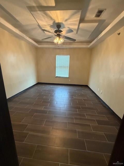 Unfurnished room featuring a raised ceiling, ceiling fan, and baseboards