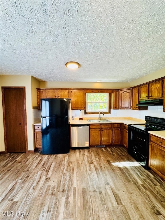 Kitchen featuring black appliances, light countertops, brown cabinetry, light wood-type flooring, and a textured ceiling