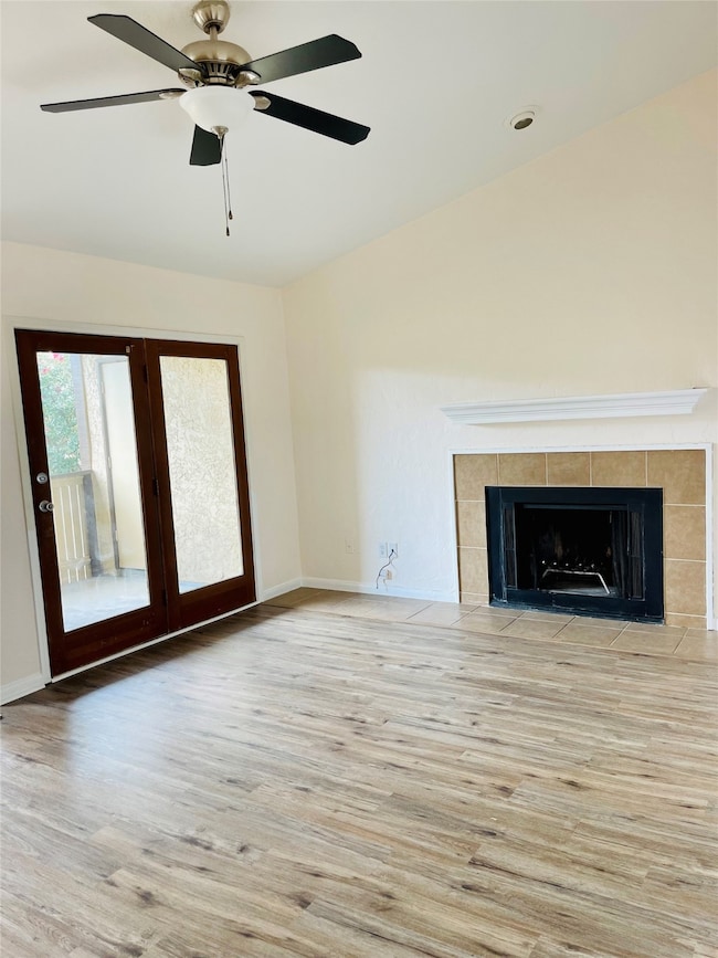 Unfurnished living room with wood finished floors, a tile fireplace, and ceiling fan