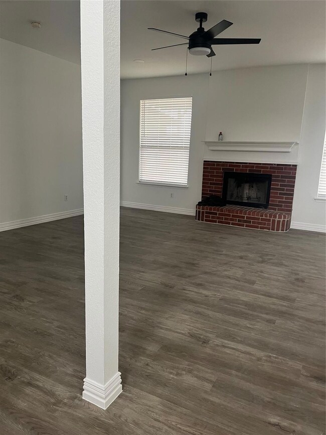 Living room featuring dark wood-type flooring, ceiling fan, and a brick fireplace