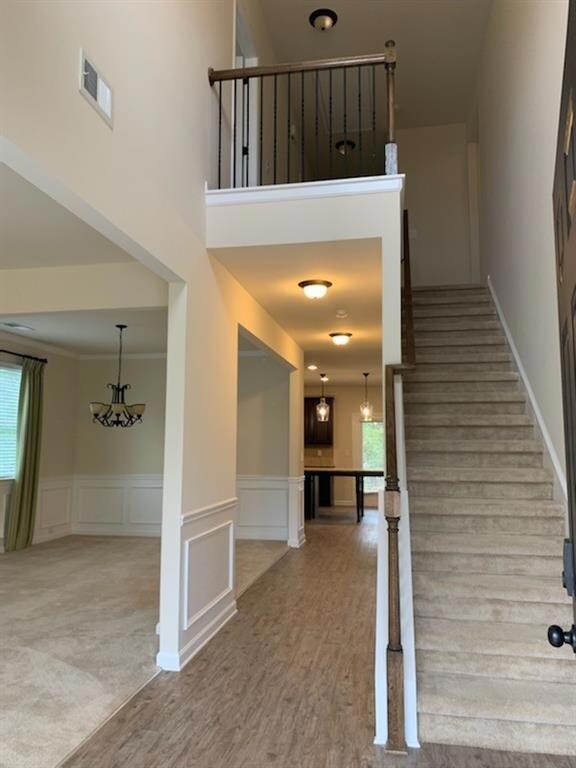Staircase featuring wood finished floors, a decorative wall, wainscoting, a chandelier, and a high ceiling