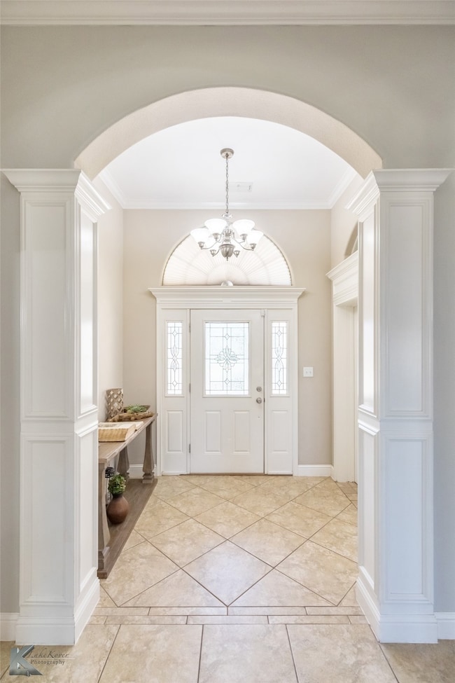 Entryway featuring light tile patterned flooring, ornamental molding, ornate columns, arched walkways, and a chandelier