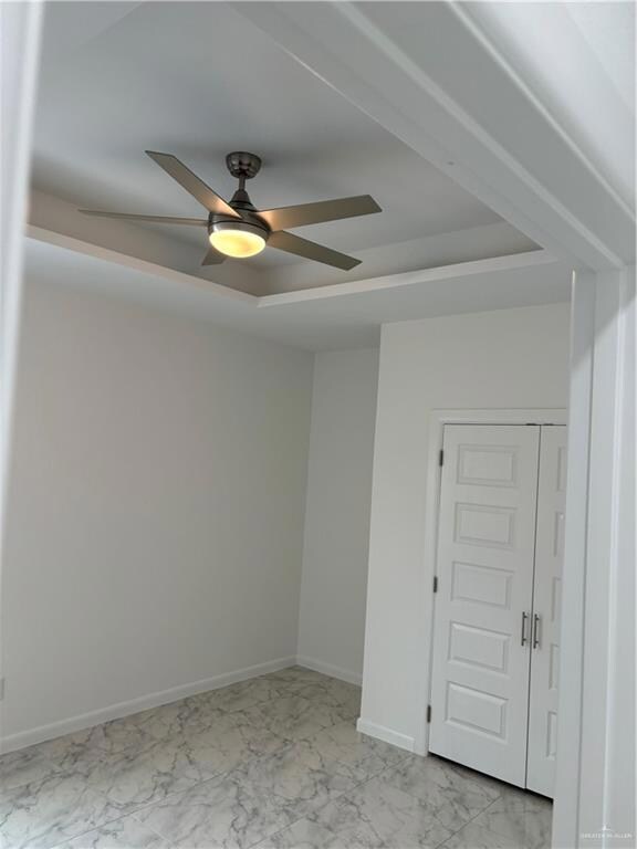 Empty room featuring light tile floors, a raised ceiling, and ceiling fan