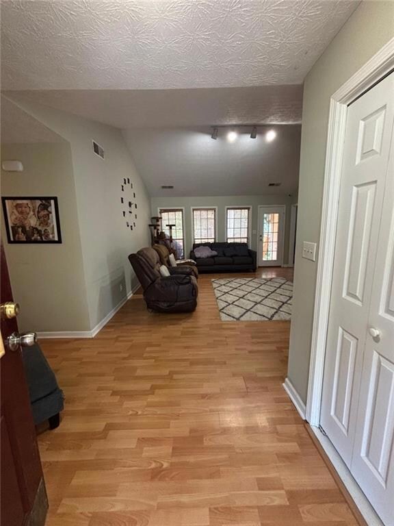 Living area with light wood-type flooring, lofted ceiling, and track lighting
