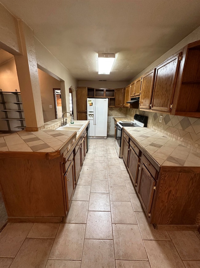 Kitchen with white fridge with ice dispenser, electric range, tile counters, and a sink