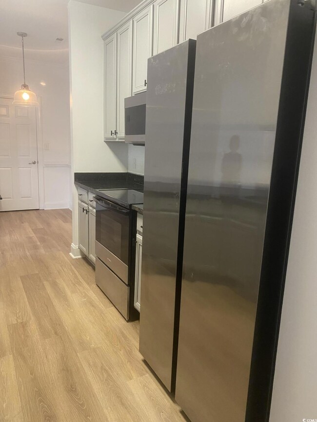 Kitchen with appliances with stainless steel finishes, light wood finished floors, and hanging light fixtures