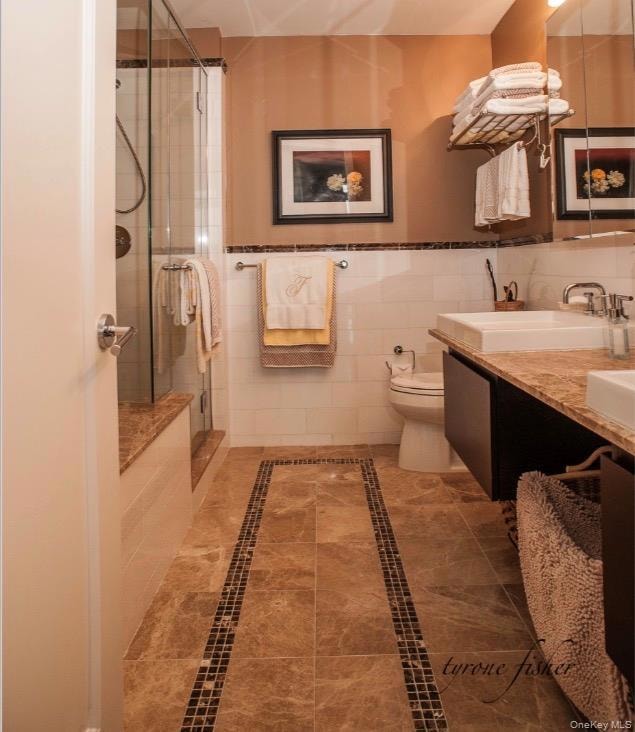 Bathroom featuring inlaid floor details, double vanity, a stall shower, tile walls, and wainscoting