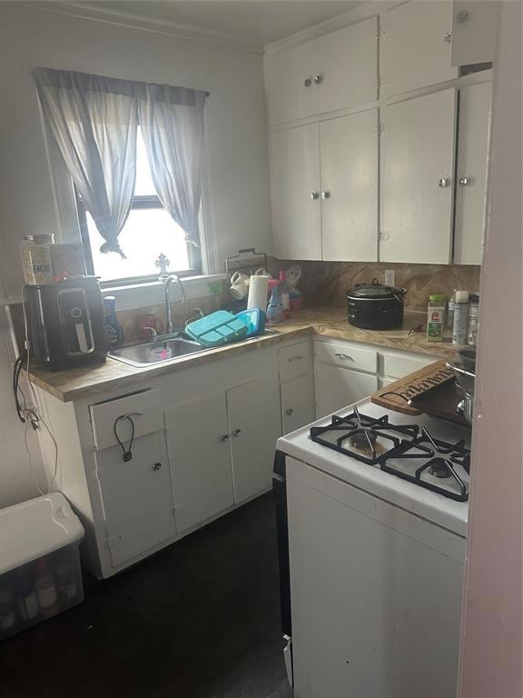 Kitchen featuring range, a sink, light countertops, white cabinetry, and crown molding