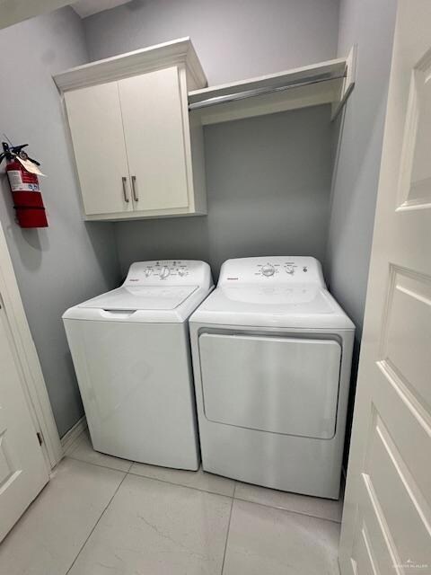 Washroom with independent washer and dryer, cabinet space, and light tile patterned floors