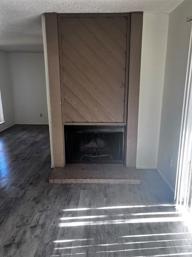 Detailed view of a brick fireplace, wood finished floors, and a textured ceiling