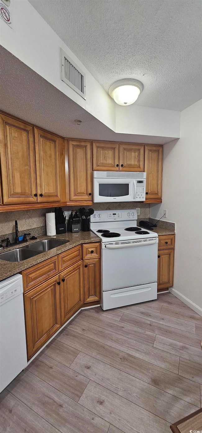 Kitchen featuring brown cabinets, white appliances, light wood-type flooring, dark stone countertops, and a textured ceiling
