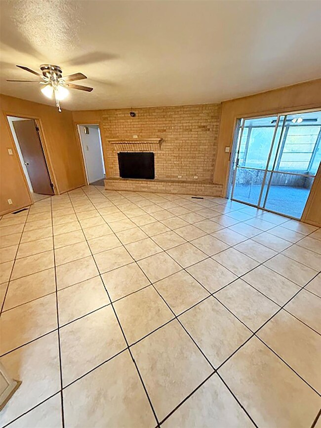 Unfurnished living room featuring a textured ceiling, light tile patterned floors, ceiling fan, brick wall, and a fireplace