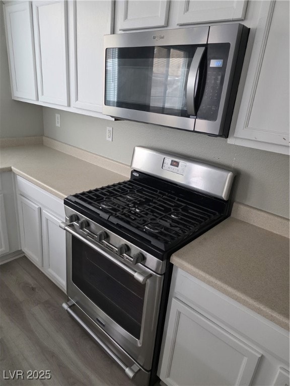 Kitchen featuring stainless steel range with gas cooktop, white cabinetry, light countertops, and dark wood finished floors