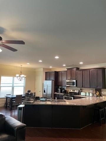 Kitchen featuring dark wood-style flooring, a breakfast bar area, stainless steel appliances, dark brown cabinets, and ornamental molding