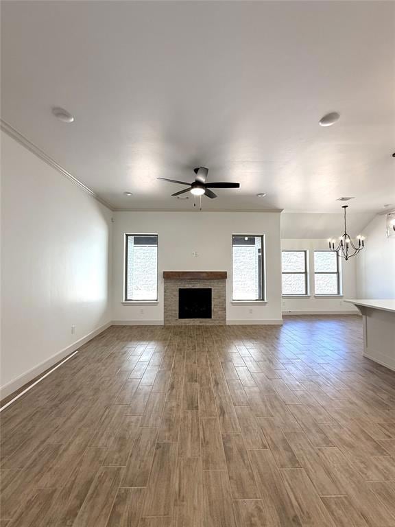 Unfurnished living room with a chandelier, a fireplace, wood finished floors, ceiling fan, and baseboards
