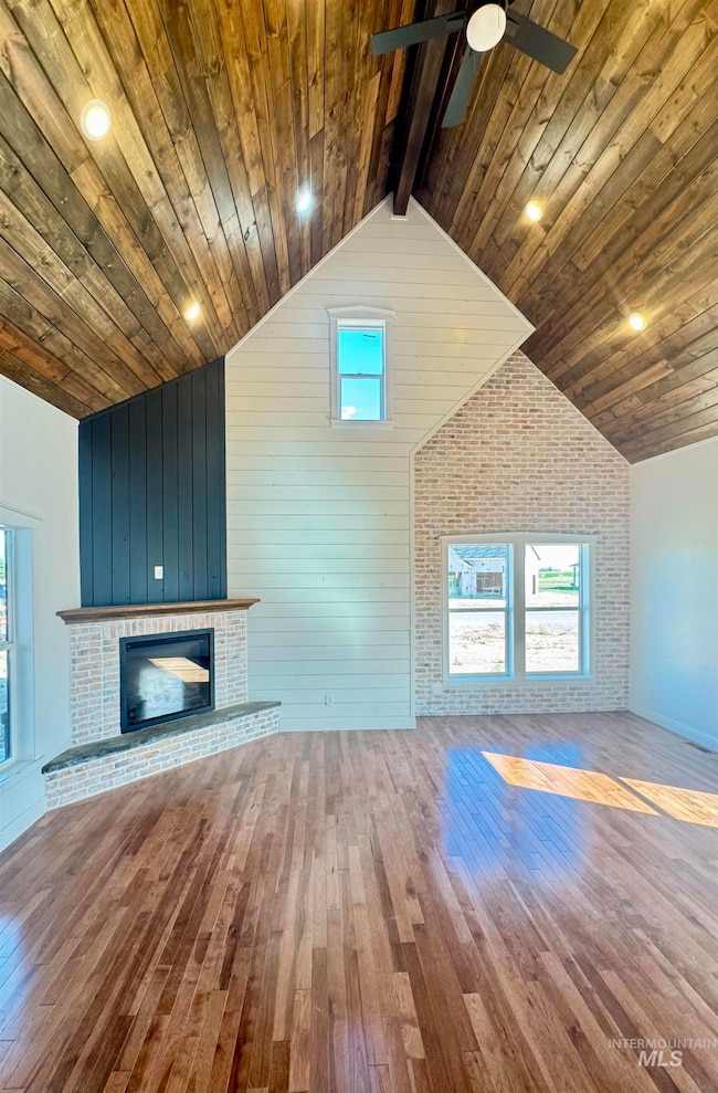 Unfurnished living room featuring a fireplace, hardwood / wood-style flooring, high vaulted ceiling, a wooden ceiling with exposed beams, and wood walls