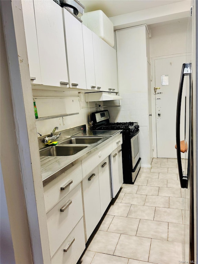 Kitchen with white cabinets, stainless steel countertops, gas range, freestanding refrigerator, and light tile patterned flooring